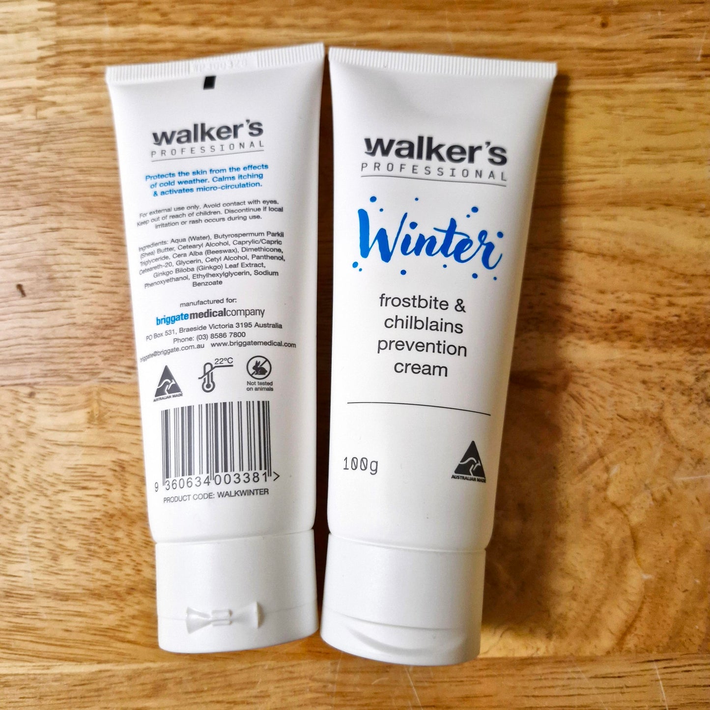 Two white squeeze tubes of Walker's Professional Winter Frostbite & Chilblains Prevention Cream placed side-by-side on a light brown wooden surface. The left tube shows the back with text and a barcode, and the right tube shows the front with the product name 'Winter' in blue script.